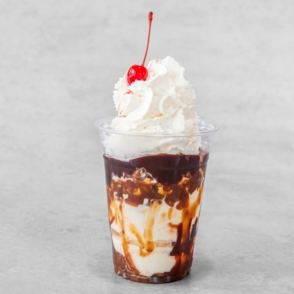 Layered chocolate and vanilla ice cream sundae in a clear cup, topped with whipped cream and a red cherry.